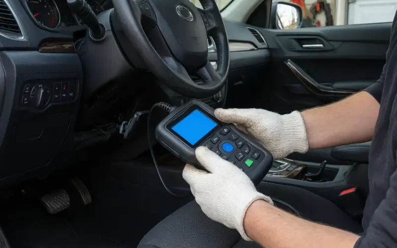 Illustration: scan tool plugged into a car's OBD port under the steering column